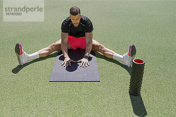 Sportler macht an einem sonnigen Tag Dehnübungen auf dem Sportplatz