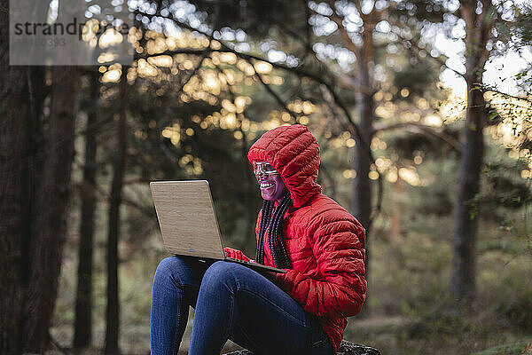 Glückliche Frau mit intelligenter Brille  die im Wald am Laptop arbeitet