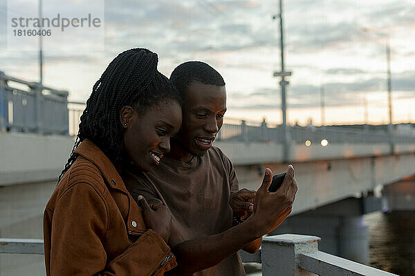 Boyfriend sharing mobile phone with girlfriend at bridge