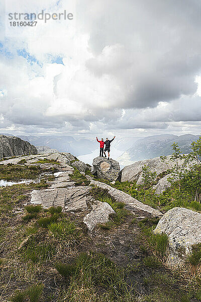 Freunde mit erhobenen Händen stehen auf einem Felsen unter Wolken