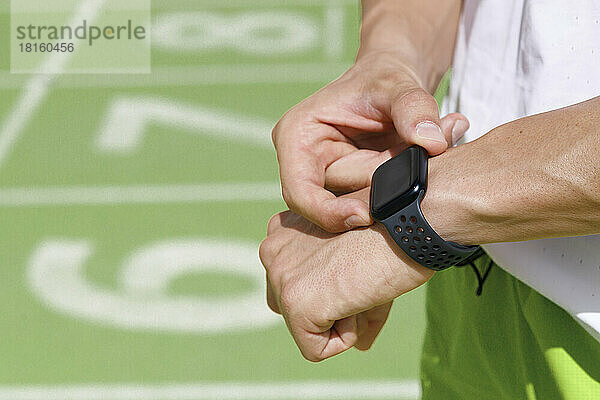 Mann überprüft Zeit auf Smartwatch an Sportstrecke