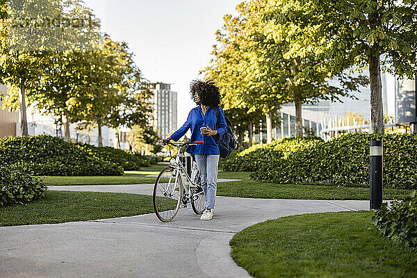 Lächelnde Frau mit Mobiltelefon und Fahrrad im Park