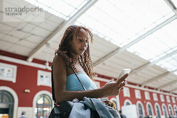 Frau benutzt Smartphone und steht am Bahnhof