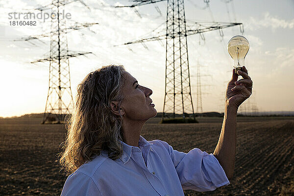 Nachdenkliche Frau blickt auf Glühbirne vor Strommasten