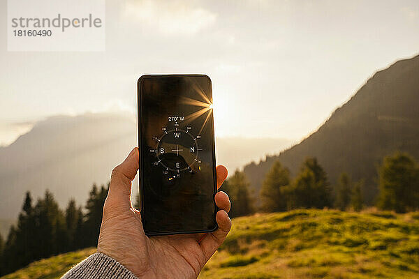 Hand eines Mannes zeigt Kompass auf Mobiltelefon