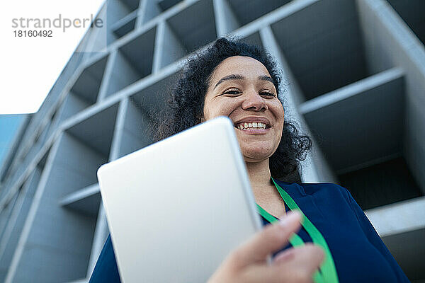 Glückliche Geschäftsfrau mit Tablet-PC vor dem Gebäude