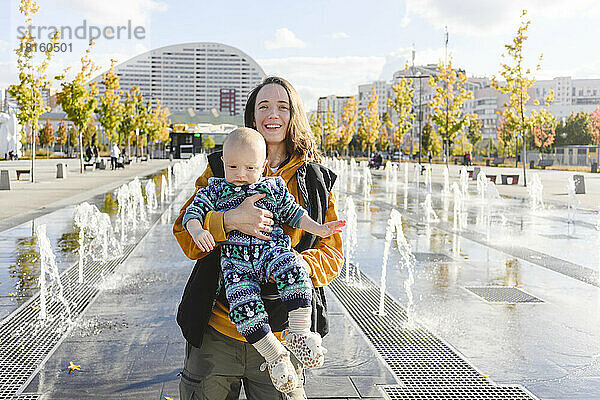 Glückliche Mutter und Sohn genießen miteinander inmitten von Springbrunnen im Stadtpark