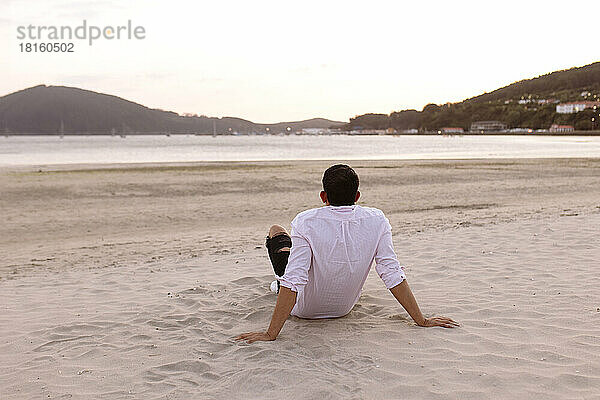 Junger Mann entspannt sich am Strand und beobachtet den Sonnenuntergang