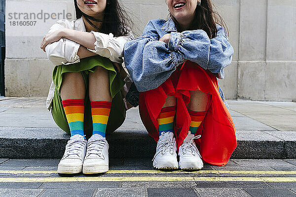 Lesbische Frauen in Schuhen und bunten Socken sitzen auf dem Fußweg