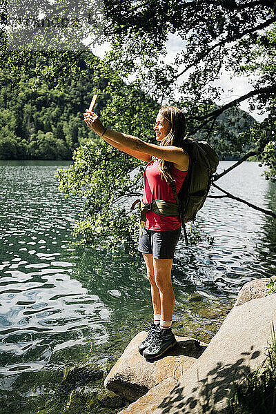 Wanderer macht ein Selfie mit seinem Smartphone und steht auf einem Felsen in der Nähe des Levico-Sees