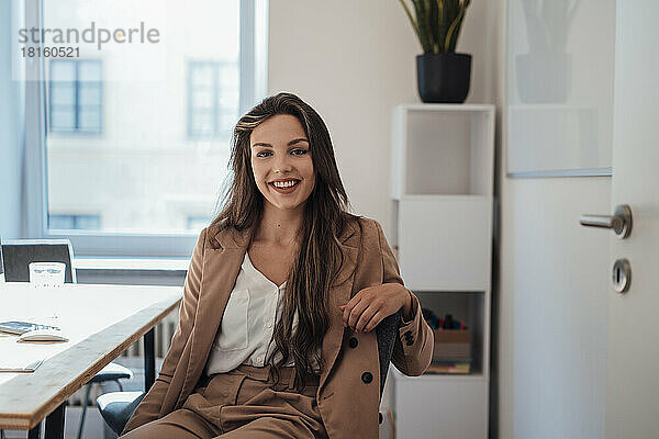 Lächelnde junge Frau mit langen Haaren sitzt im Heimbüro