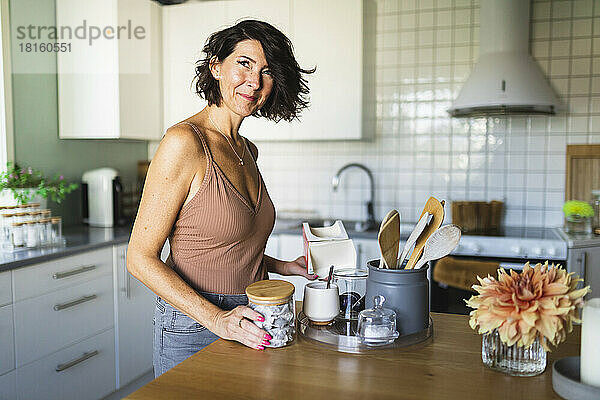 Lächelnde reife Frau vor der Kücheninsel zu Hause