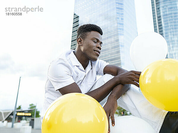 Young man with colorful balloons by modern buildings