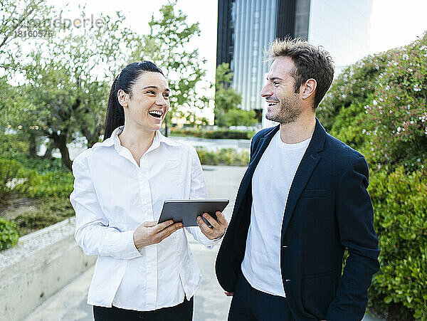 Fröhlicher Geschäftsmann mit Kollege hält Tablet-PC im Büropark