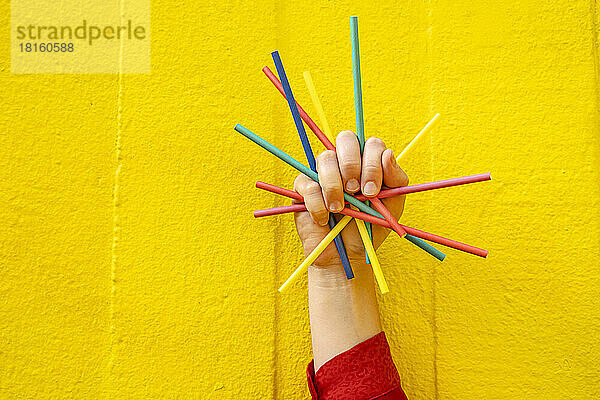 Hand einer Frau mit Buntstiften vor gelber Wand