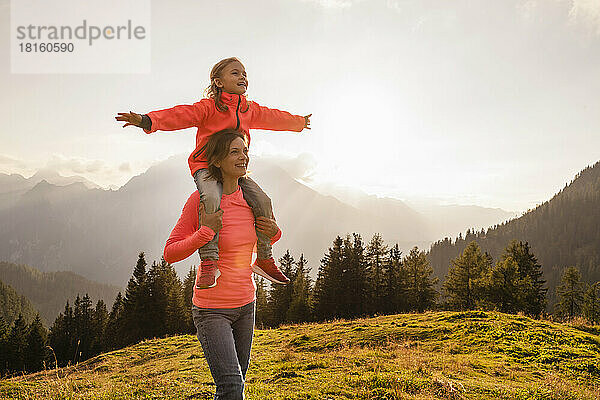 Lächelnde Mutter trägt ihre Tochter bei Sonnenuntergang auf der Schulter