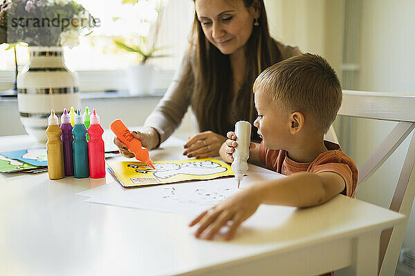 Mutter färbt mit Farbtube im Buch von Sohn zu Hause
