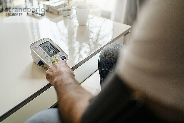 Mann benutzt Blutdruckmessgerät auf dem Tisch zu Hause