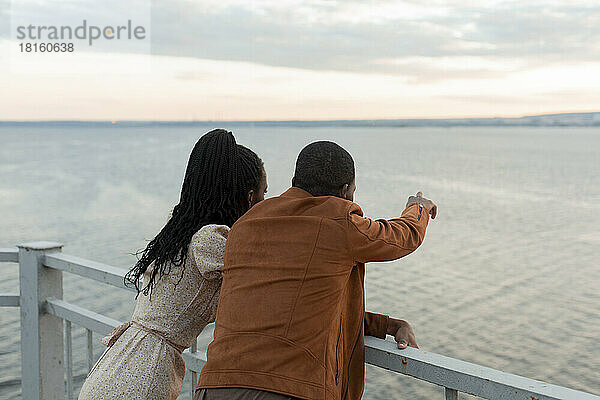 Junges Paar steht am Geländer und blickt auf den Fluss