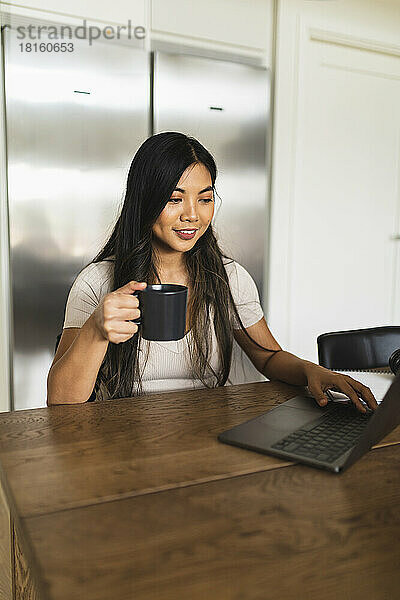 Lächelnder Freiberufler mit Kaffeetasse  der zu Hause am Laptop arbeitet