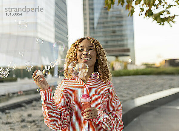 Glückliche junge Frau  die auf der Straße mit Seifenblasen spielt