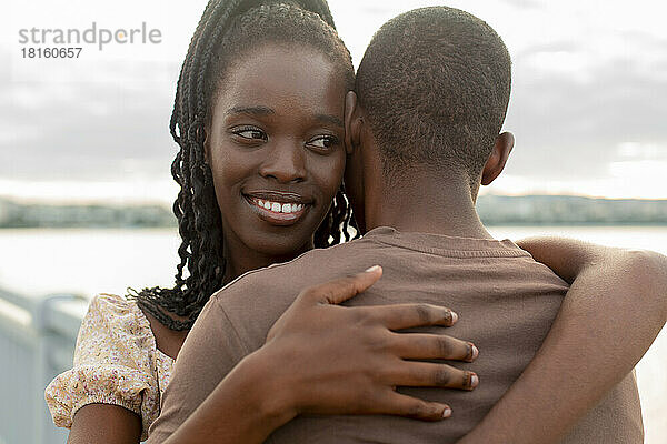 Lächelnde junge Frau umarmt ihren Freund an der Brücke