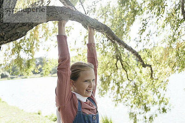 Smiling girl hanging on tree branch in park