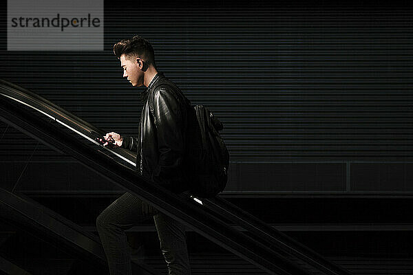 Mann benutzt Smartphone auf Rolltreppe