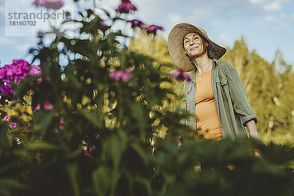 Lächelnde Frau mit Hut träumt im Garten