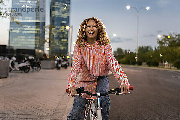 Lächelnde blonde Frau fährt Fahrrad auf der Straße in der Stadt