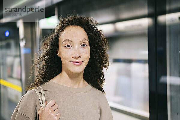 Lächelnde Frau mit lockigem Haar an der U-Bahn-Station