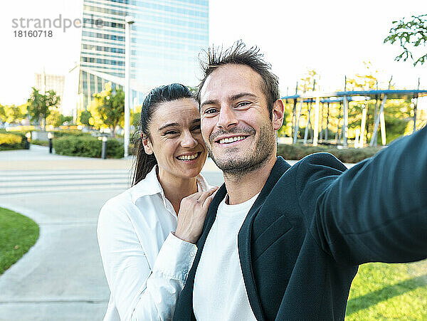Glückliche Geschäftsfrau mit Kollegin  die im Büropark ein Selfie macht