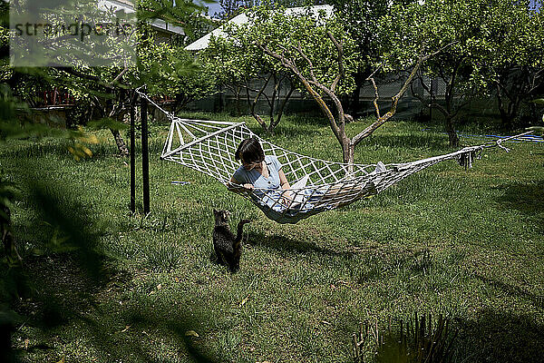Woman lying on hammock with cat in garden