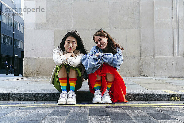 Lächelnde lesbische Freundinnen mit bunten Socken sitzen auf dem Fußweg