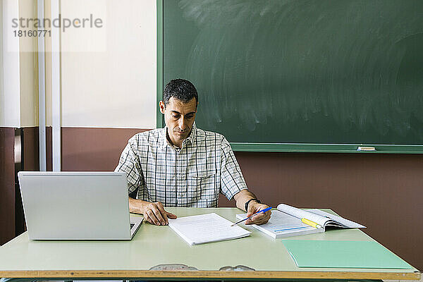 Professor sitzt mit Laptop und prüft Papier im Klassenzimmer