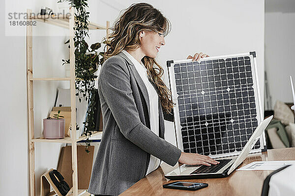 Moderne Geschäftsfrau arbeitet am Laptop und nutzt tragbares Solarmodul im Büro