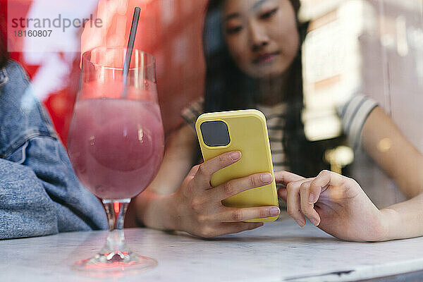 Frau benutzt Smartphone und Trinkglas auf dem Tisch im Café