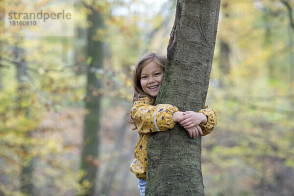 Glückliches süßes Mädchen  das einen Baum im Wald umarmt