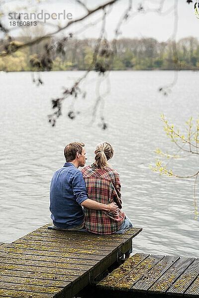 Mann mit Arm um Frau sitzt auf Steg am See