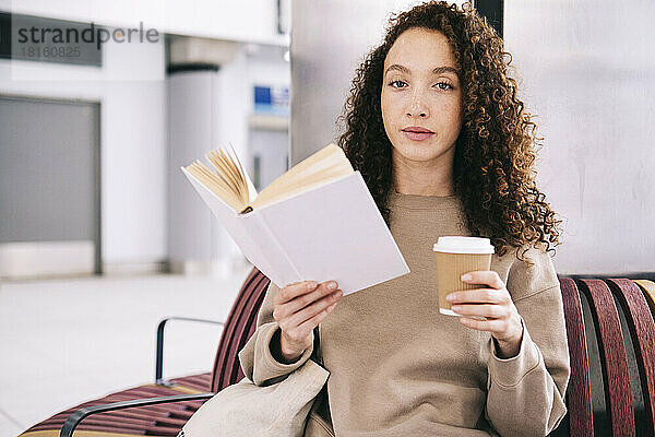 Junge Frau liest Buch mit Einwegtasse Kaffee
