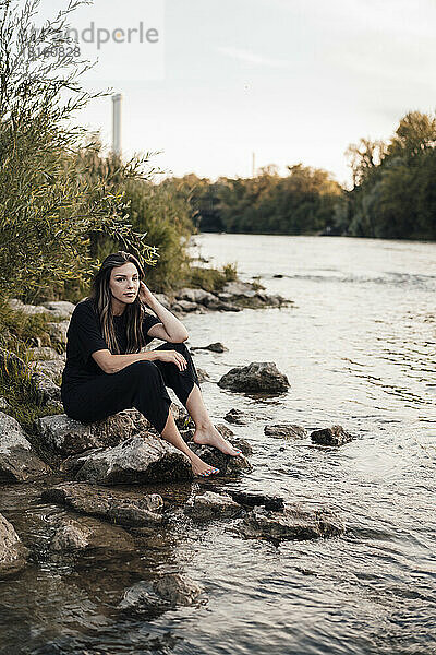 Nachdenkliche junge Frau sitzt am See