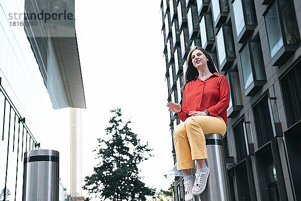 Young woman sitting on bollard in front of building