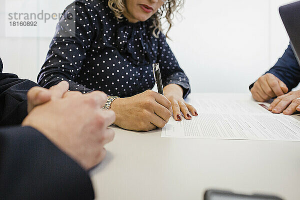 Reife Geschäftsfrau unterschreibt am Schreibtisch ein Dokument