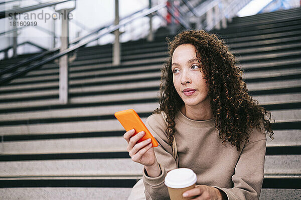 Junge Frau mit Mobiltelefon sitzt auf Stufen