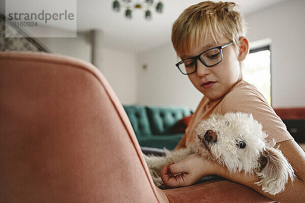 Boy with dog sitting in armchair in living room at home