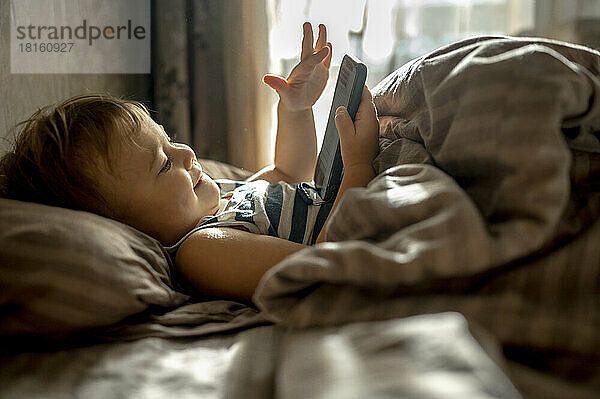 Kleiner Junge benutzt Handy zu Hause im Bett