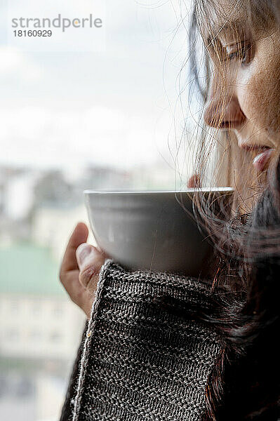 Woman wrapped in blanket holding coffee cup at home