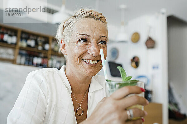 Glückliche blonde Frau mit Cocktail sitzt im Restaurant
