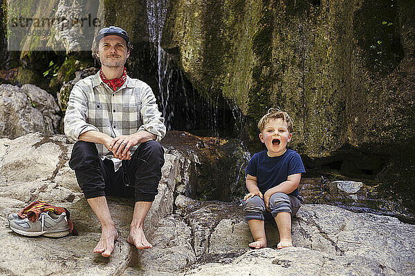 Glücklicher Junge mit Vater  der auf einem Felsen sitzt