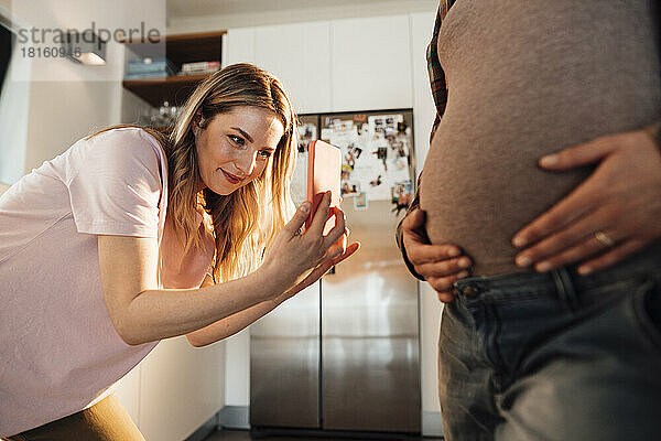 Schwester fotografiert zu Hause mit dem Handy den Bauch einer werdenden Frau